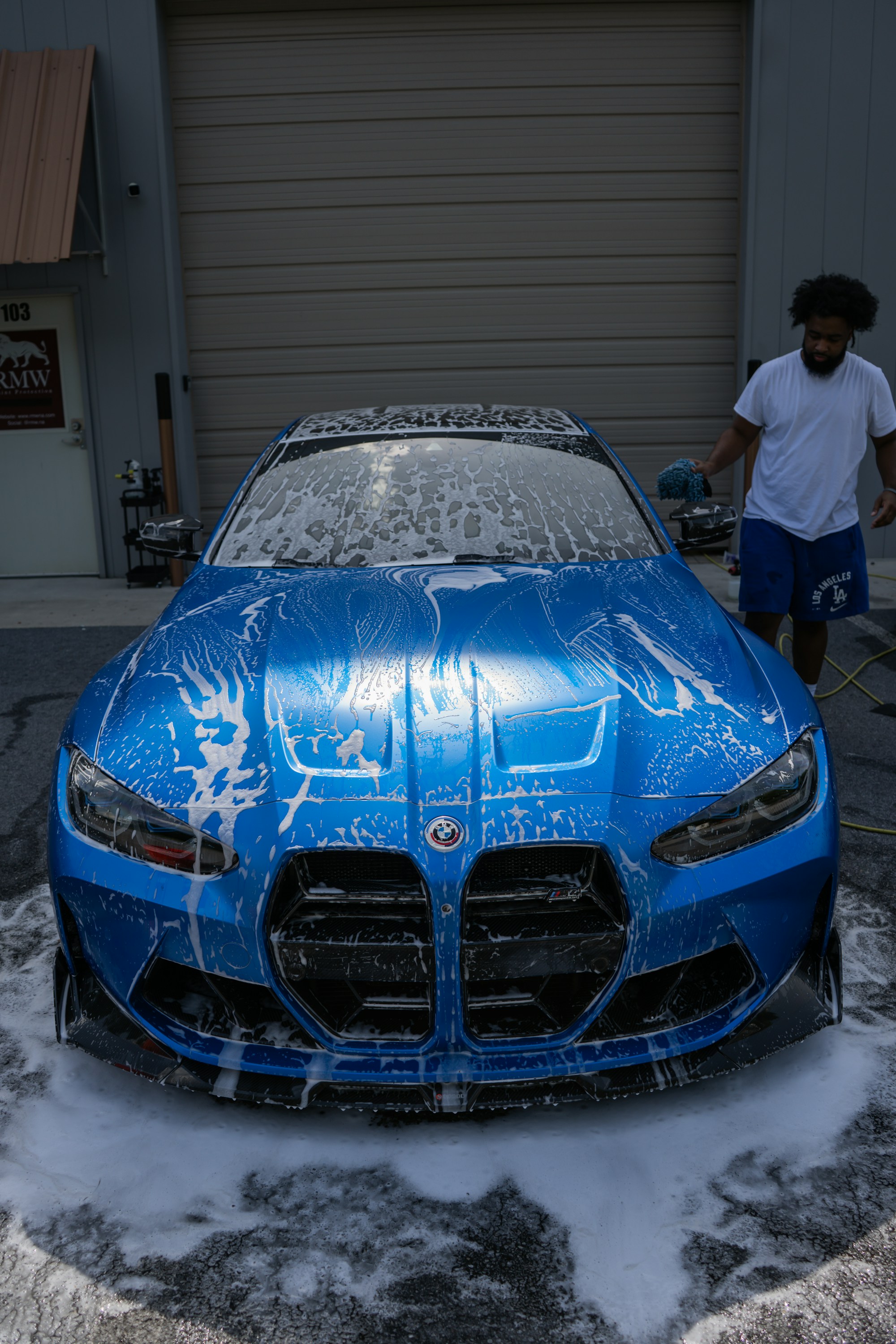 Detailer washing a blue performance car with foam
